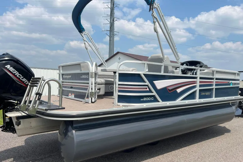 Slide: The Image of 2019 Ranger Reata 200C pontoon boat with Mercury engine, parked outdoors under blue sky. - 2