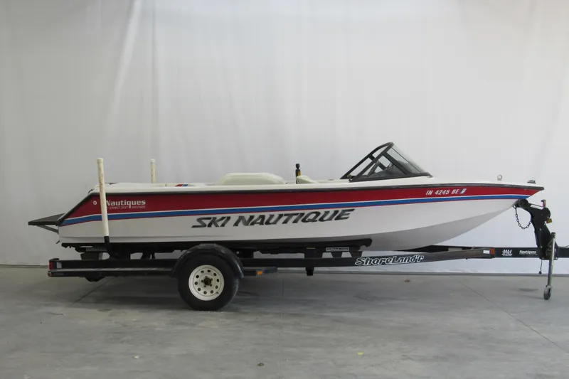 Slide: The Image of 1996 Nautique Ski 196 boat on trailer, white with red and blue accents. - 0