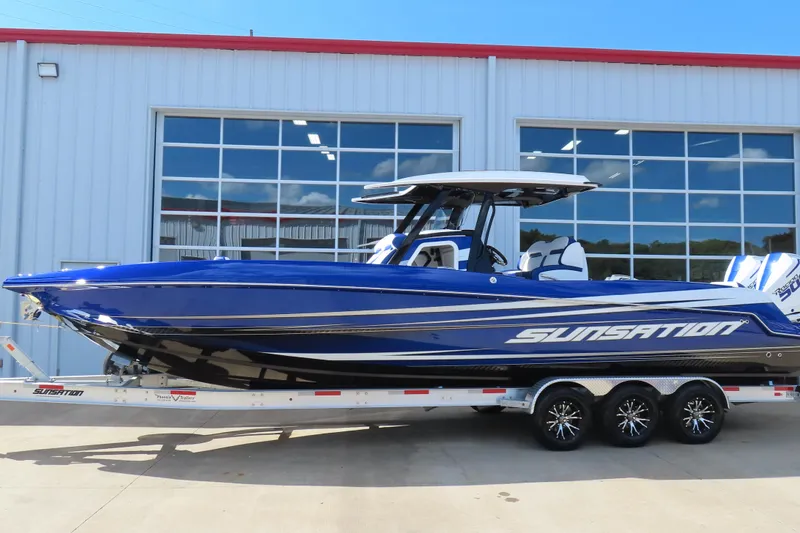 The Image of 2026 Sunsation 32CCX boat in blue on a trailer, parked outside a building. - 1