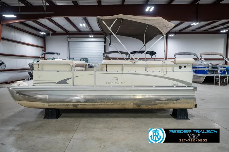 Slide: The Image of 2004 Bennington 185L pontoon boat in indoor storage, featuring a canopy and sleek design. - 10