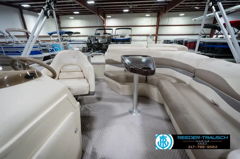 Slide: The Image of 2004 Bennington 185L pontoon boat interior with seating and table in a showroom. - 16