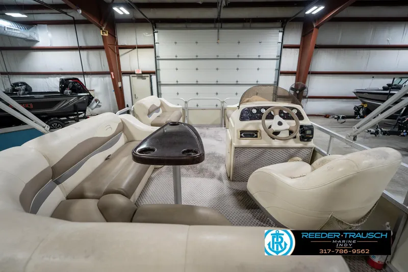 Slide: The Image of 2004 Bennington 185L pontoon boat interior with beige seating and steering console in a garage. - 17