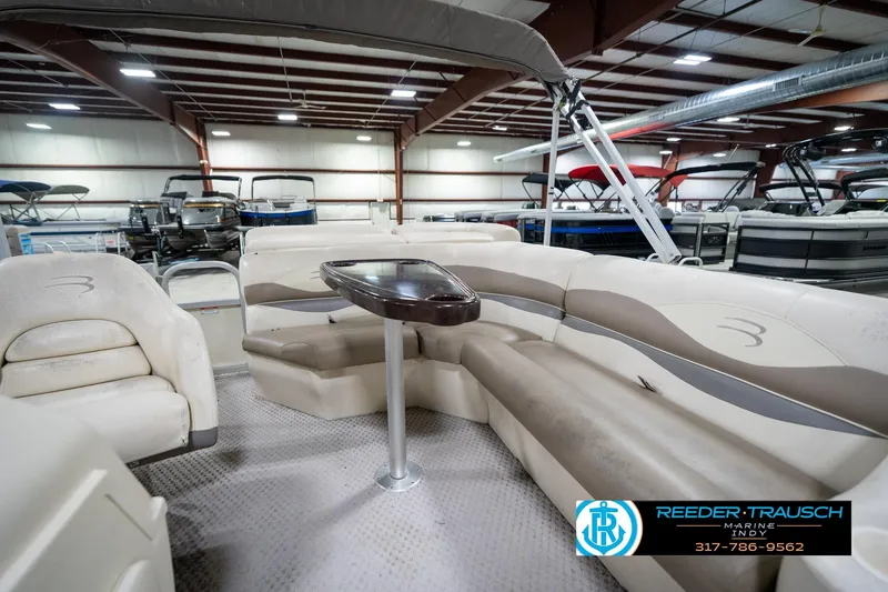 Slide: The Image of 2004 Bennington 185L pontoon boat interior with beige seating and table in showroom. - 20