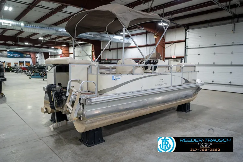 Slide: The Image of 2004 Bennington 185L pontoon boat in indoor showroom, featuring canopy and outboard motor. - 7