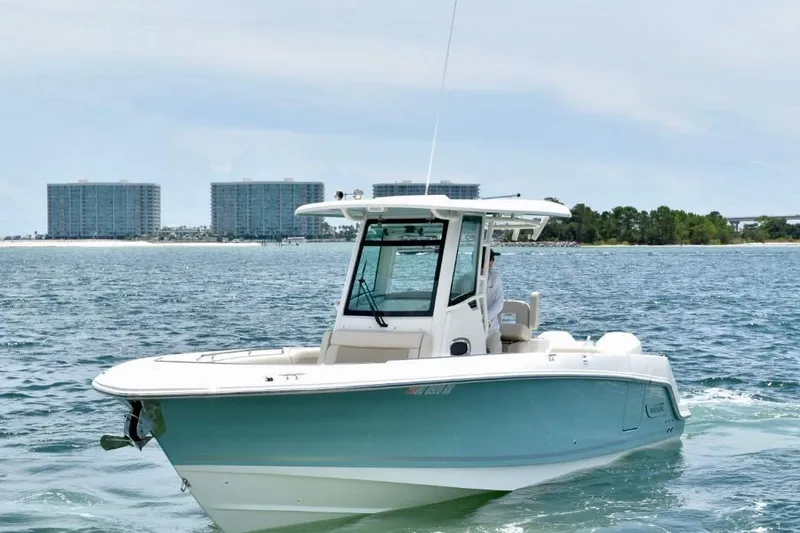 Slide: The Image of 2023 Boston Whaler 280 Outrage boat cruising on open water near coastal buildings. - 1