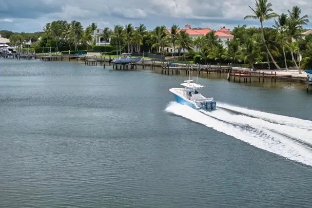 Slide: The Image of Invincible 36 boat cruising on a scenic waterway, surrounded by palm trees and waterfront homes. - 59