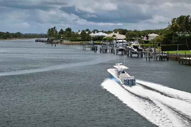 Slide: The Image of A 2015 Invincible 36 boat cruising on a scenic waterfront with docks and palm trees. - 60