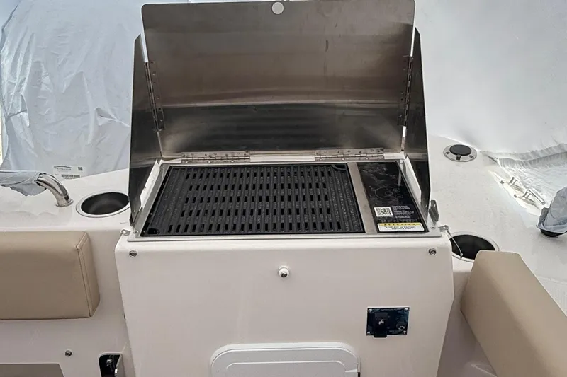 Slide: The Image of 2025 Ranger Tugs R-25 boat grill setup with stainless steel cover and seating area. - 7