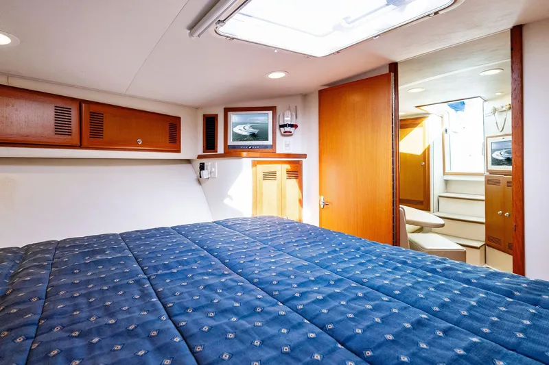 Slide: The Image of 2004 Cabo 40 Hardtop Express cabin interior with blue bedding and wooden accents. - 32