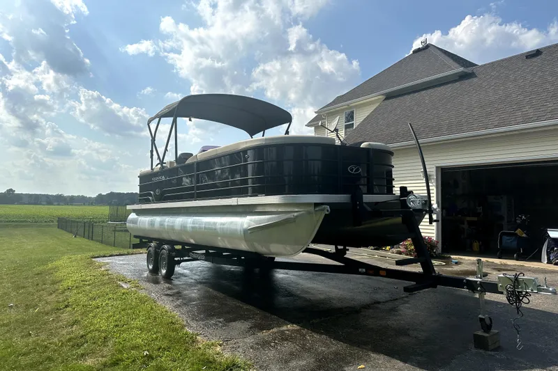Slide: The Image of 2021 Veranda Vista 22RC pontoon boat on trailer beside a house under a sunny sky. - 5
