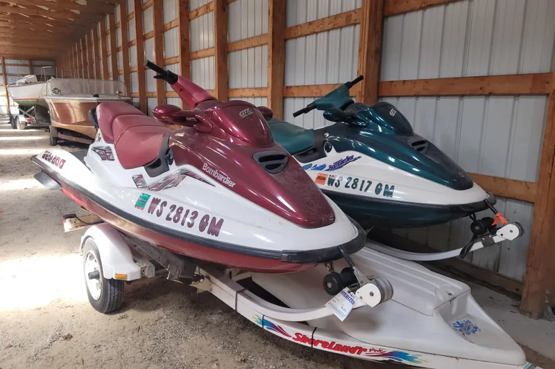 Slide: The Image of 1998 SkiDoo GTX jet skis in storage, red and green models on a trailer. - 1
