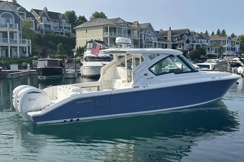 Slide: The Image of 2024 Pursuit DC 326 Dual Console boat docked in a scenic marina setting. - 0