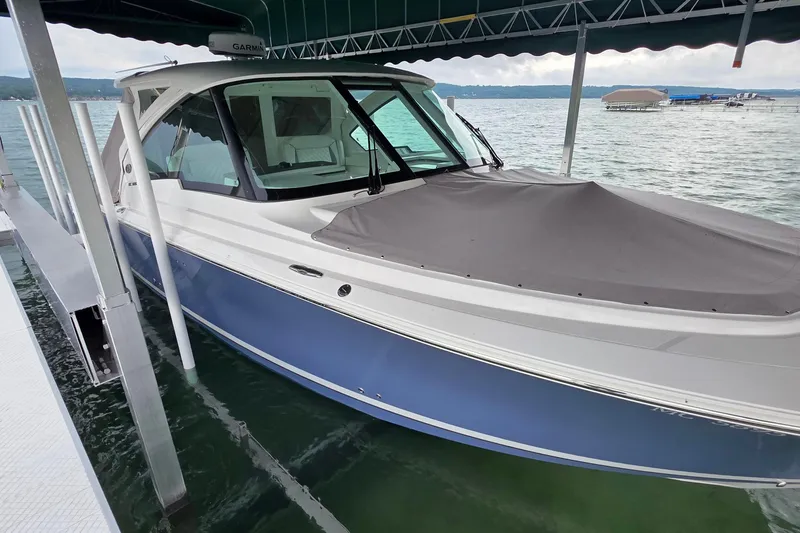 Slide: The Image of 2024 Pursuit DC 326 Dual Console boat docked on a lake under a canopy. - 1