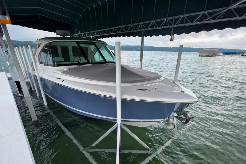 Slide: The Image of 2024 Pursuit DC 326 Dual Console boat docked under a canopy on a lake. - 2