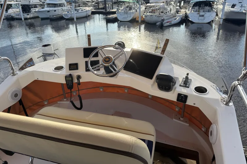 Slide: The Image of 2024 Ranger Tugs R31CB helm with steering wheel, controls, and marina view. - 12