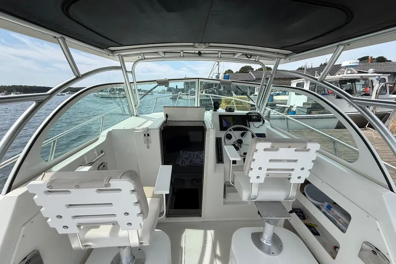 Slide: The Image of 2015 Parker 2510 XLD Walkaround boat interior with helm and seating, docked by the water. - 10