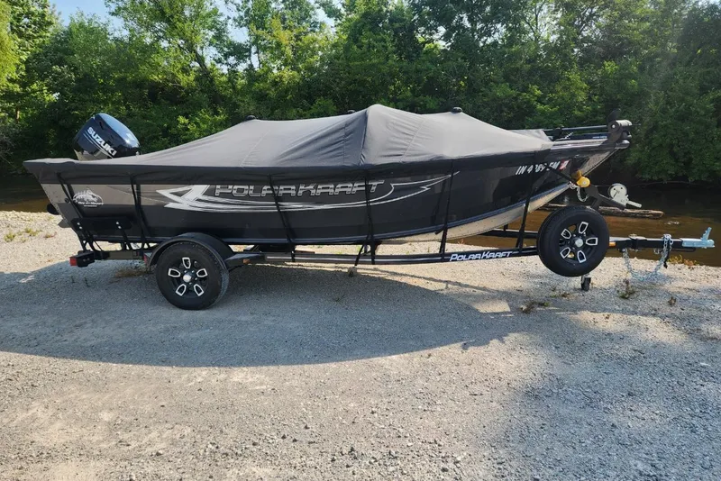 Slide: The Image of 2024 Polar Kraft Frontier 165 SCJ boat on trailer, covered, near a riverbank. - 22