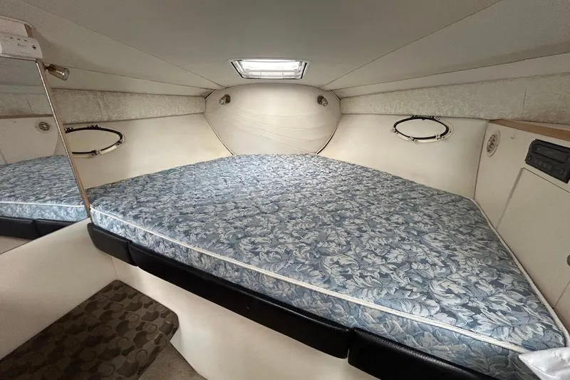 Slide: The Image of 2001 Larson Cabrio 330 cabin interior with floral-patterned bed and porthole windows. - 13
