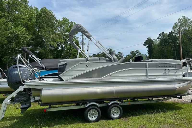 Slide: The Image of 2025 Bennington 22M pontoon boat on trailer, parked outdoors with trees in background. - 3