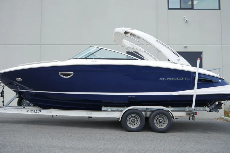 Slide: The Image of 2018 Regal 2800 Bowrider boat on trailer, sleek blue design, parked outdoors. - 4