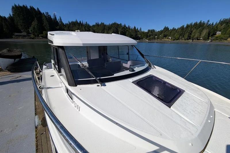 Slide: The Image of 2020 Jeanneau NC 695 Series 2 boat docked on a serene lake with forested background. - 2