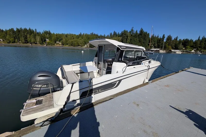 Slide: The Image of 2020 Jeanneau NC 695 Series 2 boat docked on a serene lake with forest backdrop. - 3