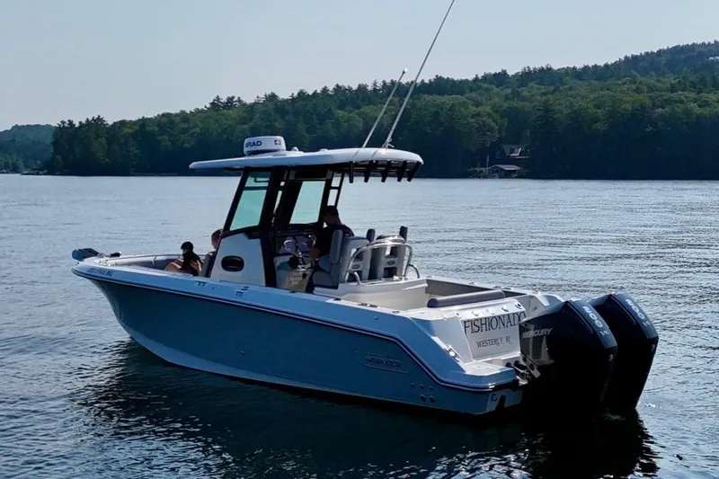 Slide: The Image of 2024 Boston Whaler 250 Outrage boat on a serene lake with lush forest backdrop. - 3