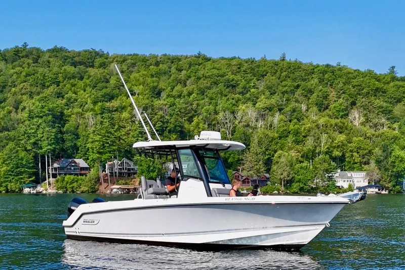 Slide: The Image of 2024 Boston Whaler 250 Outrage boat on a scenic lake with lush green forest backdrop. - 5