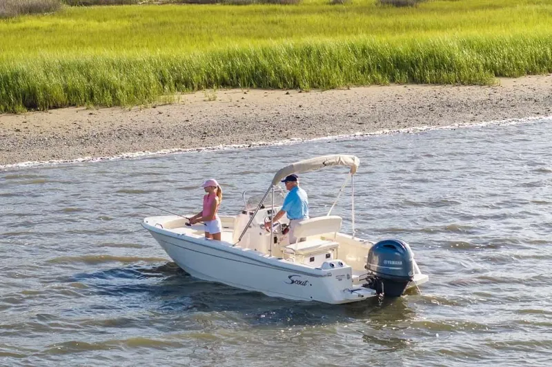 Slide: The Image of 2026 Scout 188 Sportfish boat on water near grassy shoreline, two people fishing. - 18