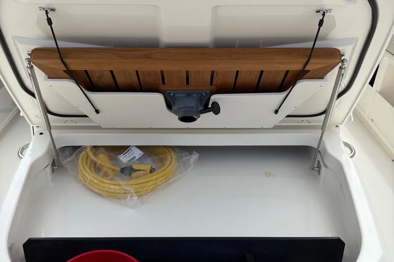 Slide: The Image of Storage compartment on a 2025 Boston Whaler 360 Outrage with coiled yellow hose. - 16