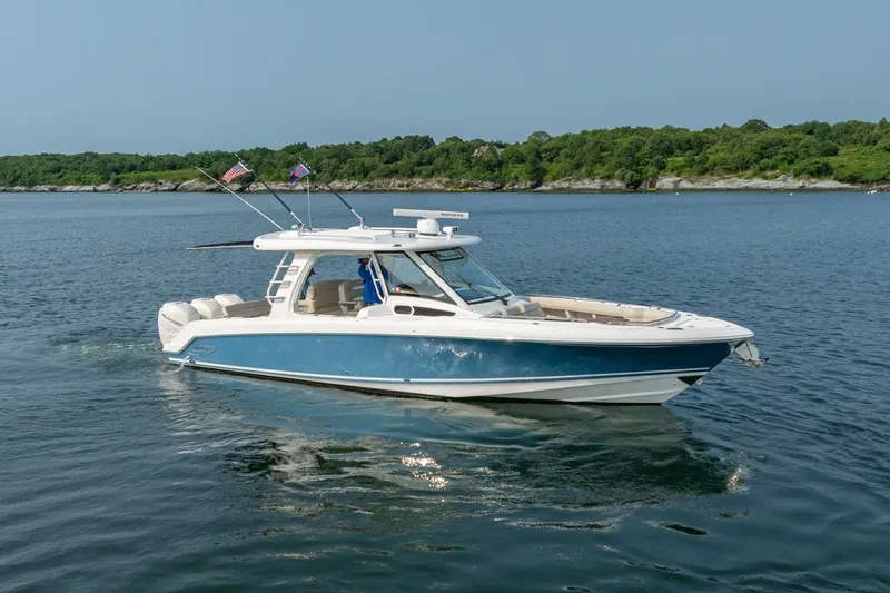 The Image of 2019 Boston Whaler 350 EX REALM boat cruising on calm water with lush green shoreline. - 1