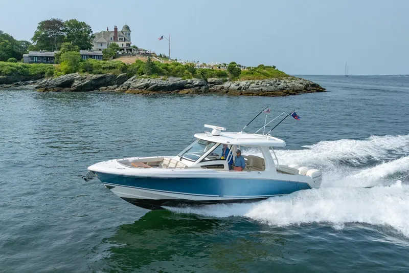Slide: The Image of 2019 Boston Whaler 350 EX REALM cruising near rocky shoreline and coastal estate. - 48