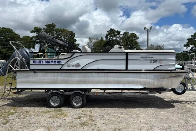 Slide: The Image of 2022 Sun Catcher 322 SS pontoon boat on trailer, labeled "White Diamond," outdoors. - 2