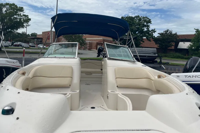 Slide: The Image of 2001 Sea Ray 210 Sundeck boat with beige seating and blue canopy in a parking lot. - 2