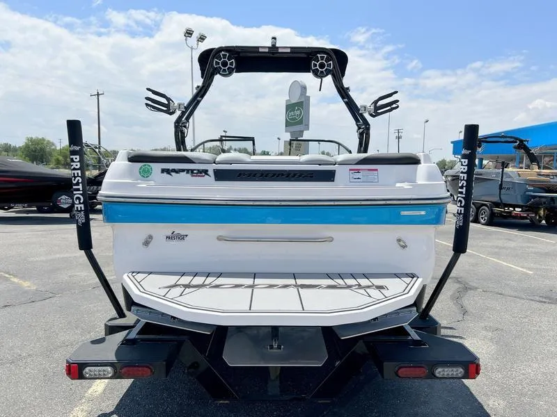 Slide: The Image of 2018 Moomba Mojo™ boat rear view in parking lot, featuring wakeboard tower and swim platform. - 9