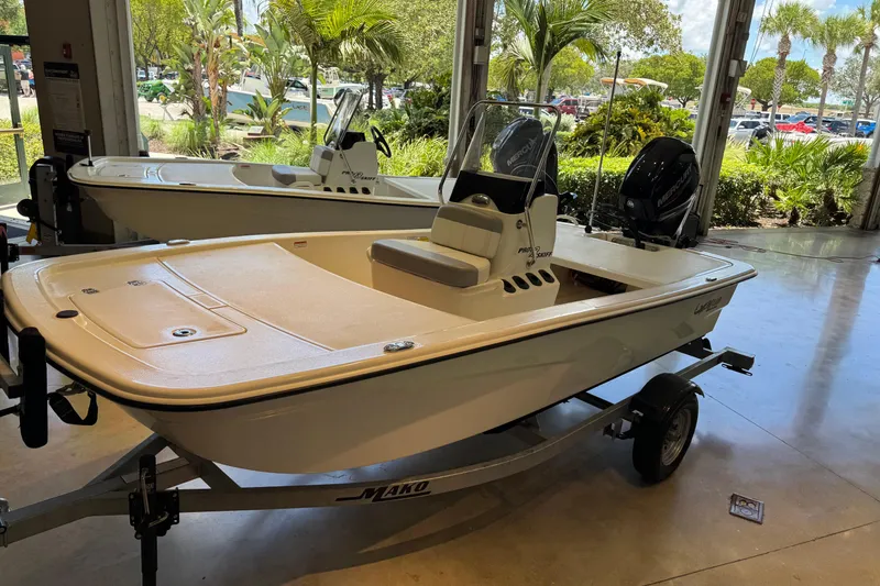 Slide: The Image of 2024 Mako 13 Pro Skiff CC boat displayed indoors with lush greenery outside. - 5