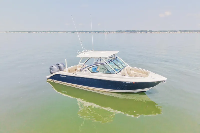 Slide: The Image of 2023 Pursuit DC 266 Dual Console boat on calm water, clear sky background. - 0