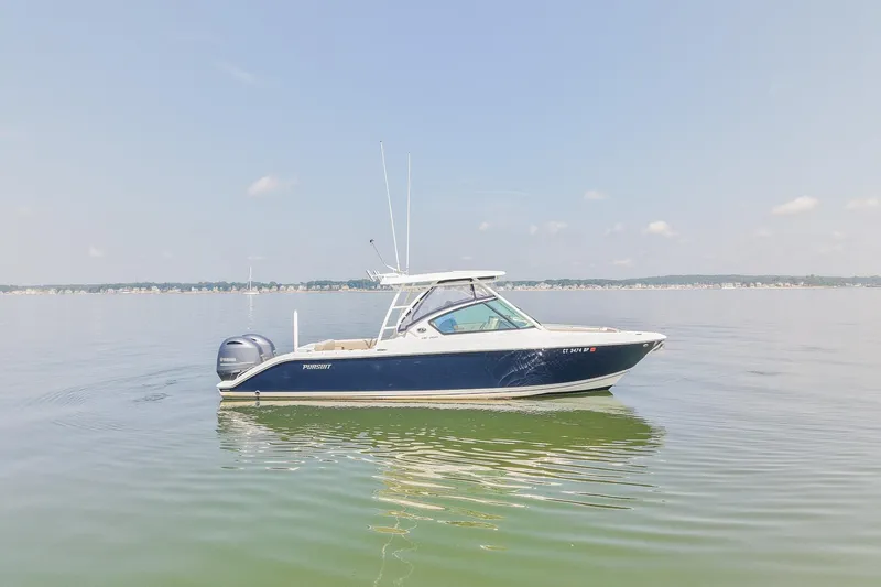 Slide: The Image of 2023 Pursuit DC 266 Dual Console boat on calm water under clear sky. - 2