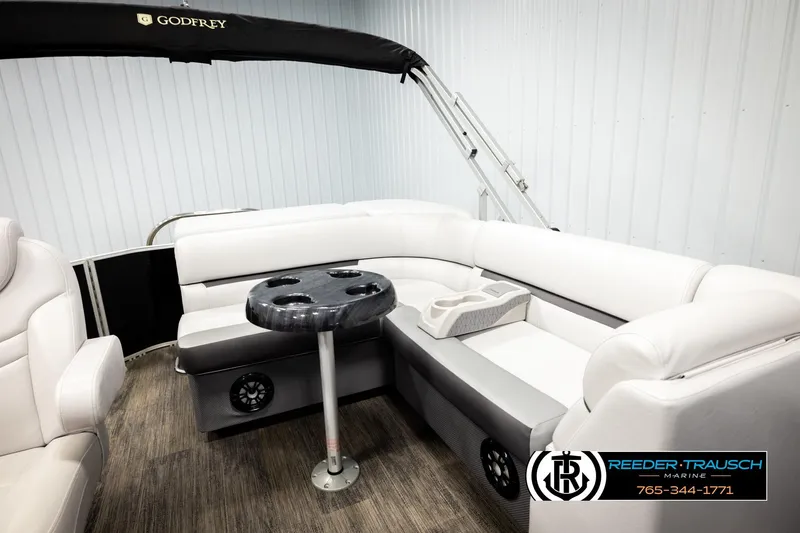 Slide: The Image of 2023 Godfrey SW2286C pontoon boat interior with white seating and table, Reeder-Trausch Marine logo. - 22