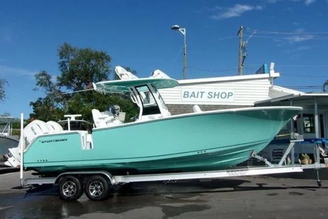 Slide: The Image of 2025 Sportsman Heritage 261 boat on trailer near bait shop, clear sky background. - 0