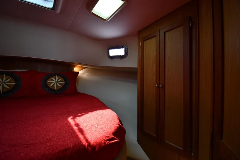 Slide: The Image of Cozy cabin interior of 2006 Mainship 40 Trawler with red bedding and wooden cabinetry. - 40