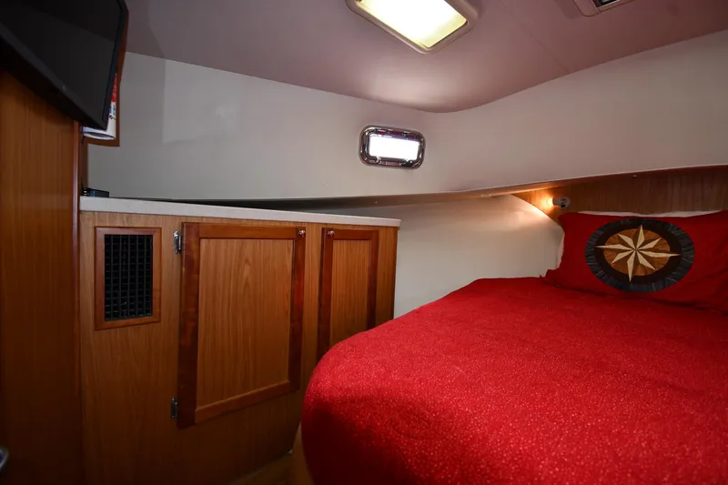 Slide: The Image of Cozy cabin interior of 2006 Mainship 40 Trawler with red bedding and wooden cabinets. - 41