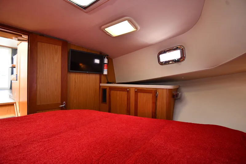 Slide: The Image of 2006 Mainship 40 Trawler cabin interior with red bedding, TV, and wooden cabinetry. - 42