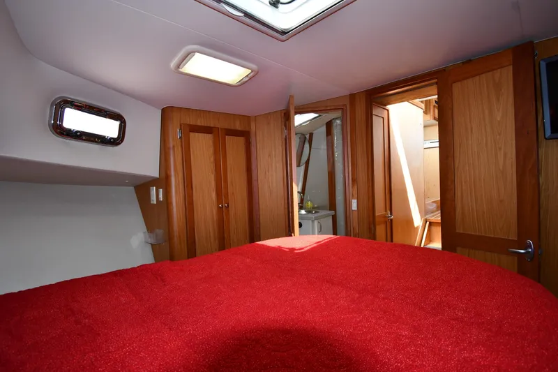 Slide: The Image of Interior of 2006 Mainship 40 Trawler with red bedding and wooden cabinetry. - 43