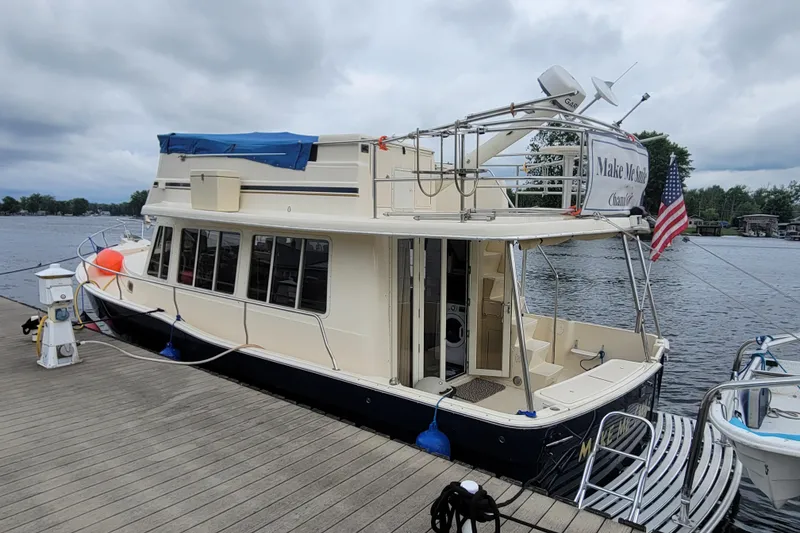 Slide: The Image of 2006 Mainship 40 Trawler docked by a lake, featuring an American flag and blue canopy. - 96