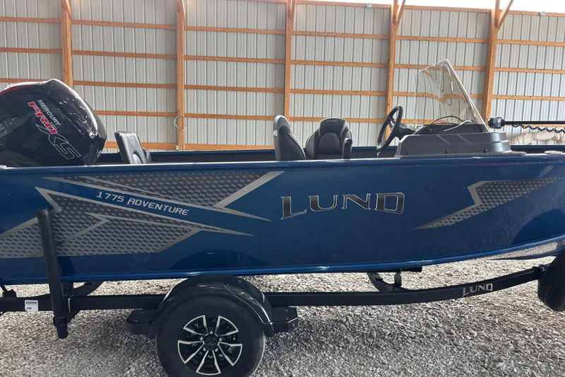 Slide: The Image of 2026 Lund 1775 Adventure SS boat in a storage facility, featuring a sleek blue design. - 1