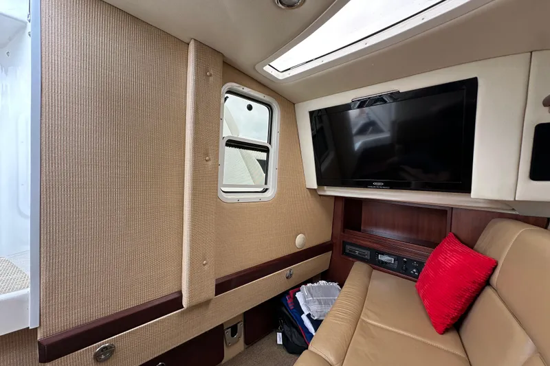 Slide: The Image of Interior of 2015 Cobalt 336 boat with TV, beige seating, and red pillow. - 24
