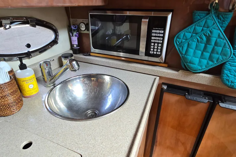 Slide: The Image of 2003 Regal Commodore 4260 yacht kitchen with sink, microwave, and teal oven mitts. - 49