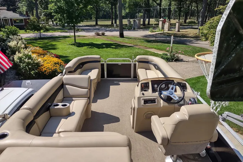 Slide: The Image of 2013 Bennington 22 SSX pontoon boat with beige seating and steering wheel, parked near garden. - 3
