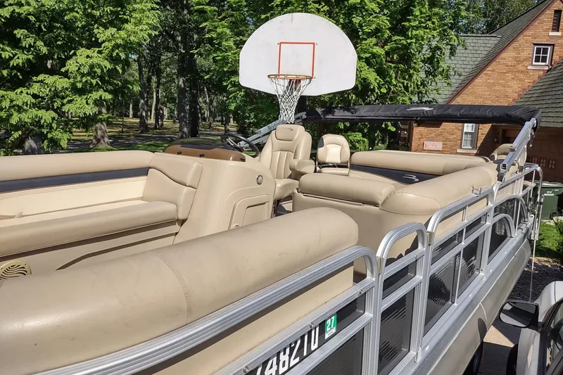 Slide: The Image of 2013 Bennington 22 SSX pontoon boat parked near a basketball hoop, surrounded by trees. - 9